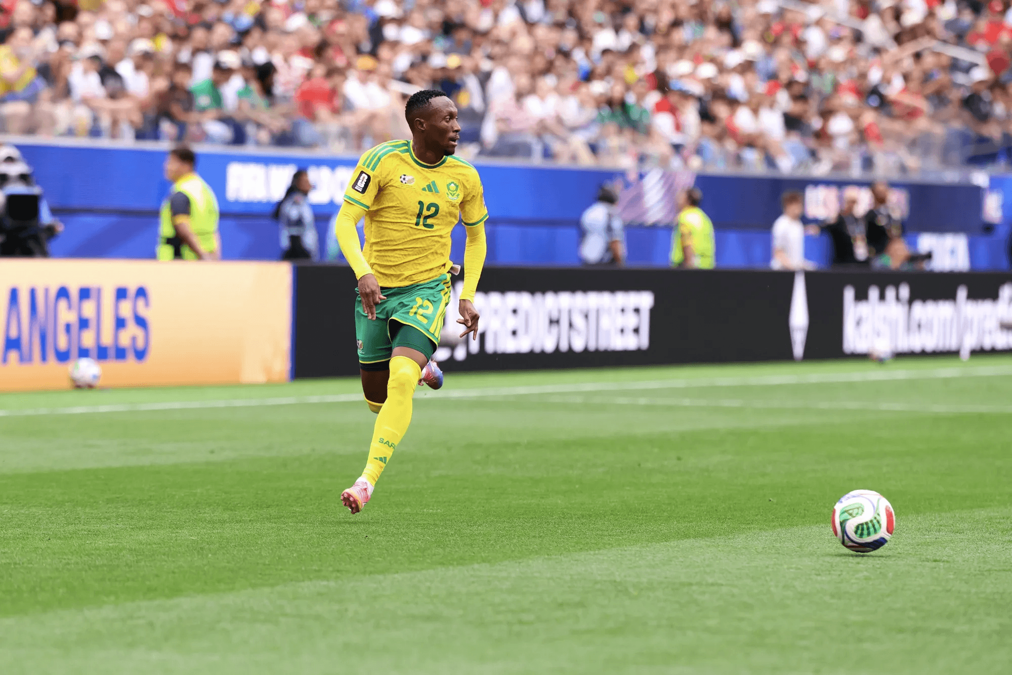 South Africa player number 12 advances toward the ball during a 2026 World Cup match at Los Angeles Stadium, with prediction-market advertising along the pitch.